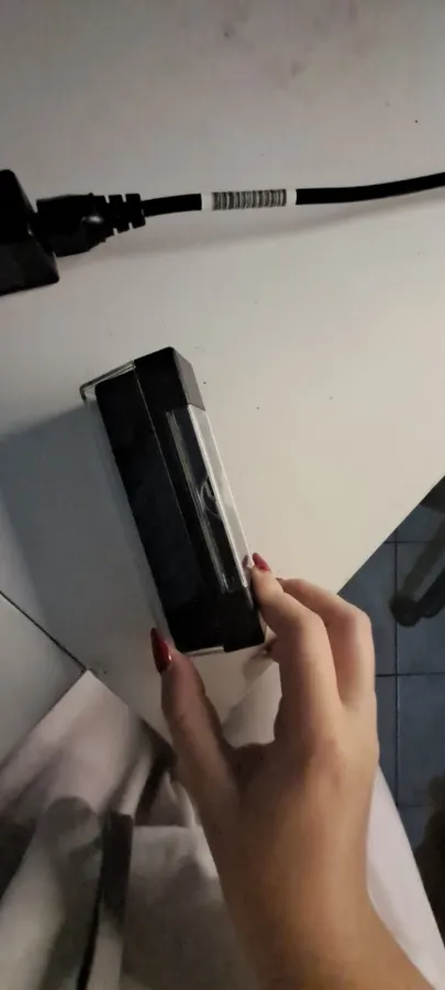 Hand holding the velvet block over a white surface, with a power cable running along the wall behind
